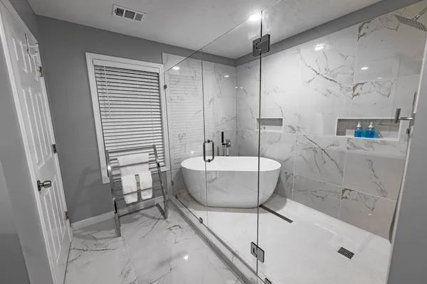 Completed bathroom with freestanding tub, glass shower and marble-pattern wall tile
