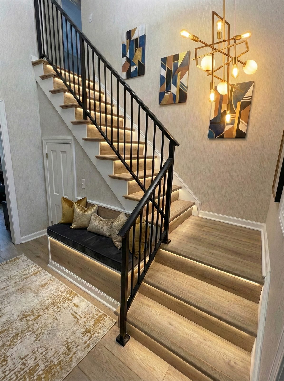 Remodeled staircase with black iron railing, wood treads, and brass chandelier
