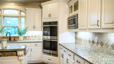 Wall ovens framed by refinished white cabinetry and tile backsplash