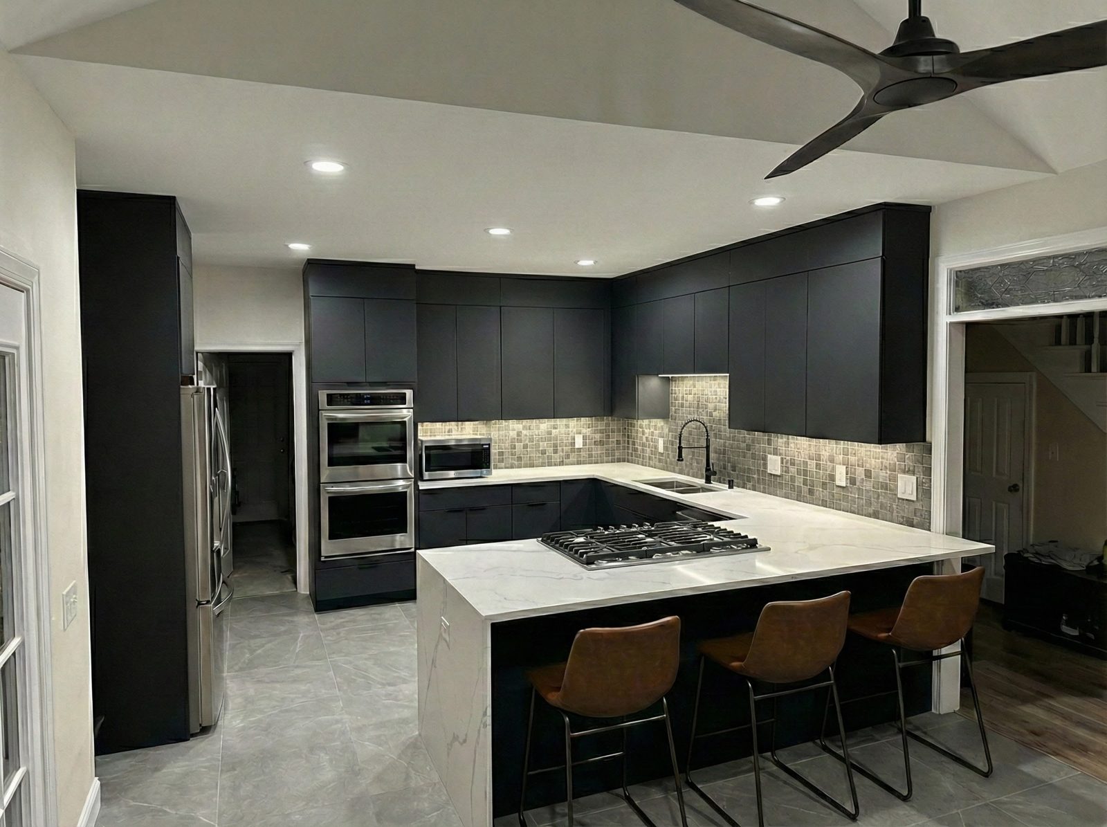 Modern kitchen with charcoal cabinetry, waterfall island, and stainless wall ovens