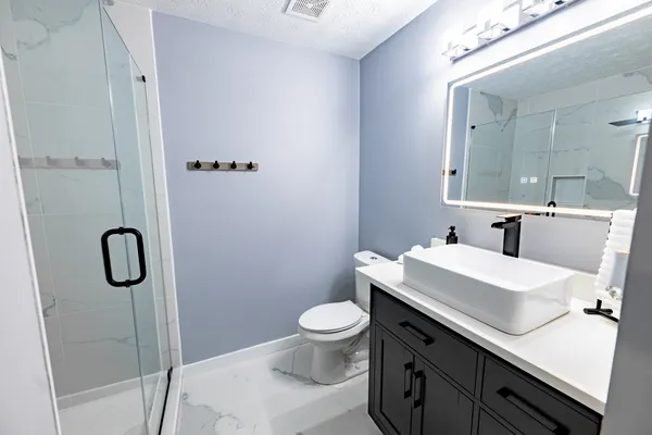 Completed bathroom with glass shower, vessel sink, dark vanity and illuminated mirror
