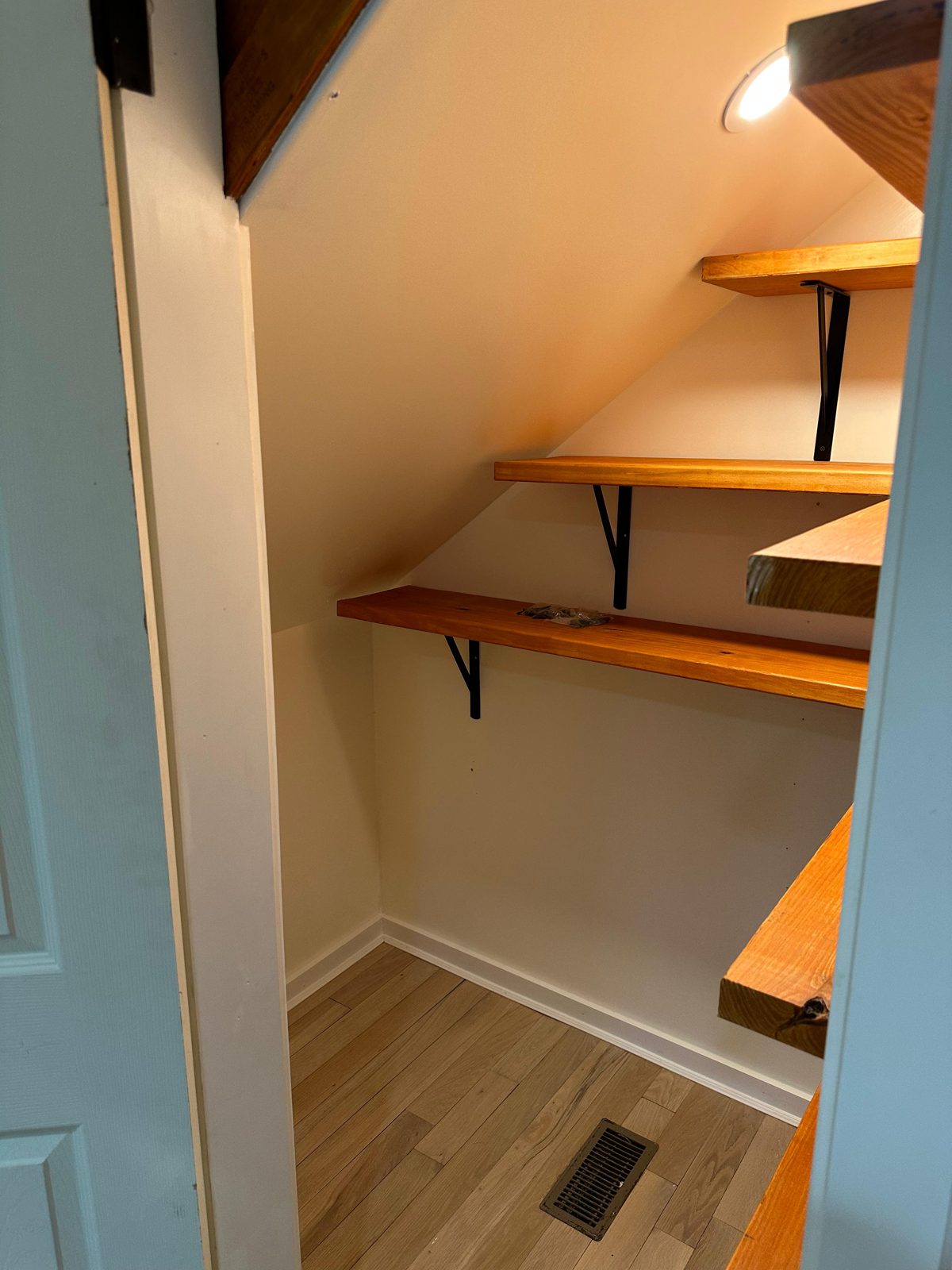 Custom wood shelving built into an under-stair closet with iron brackets